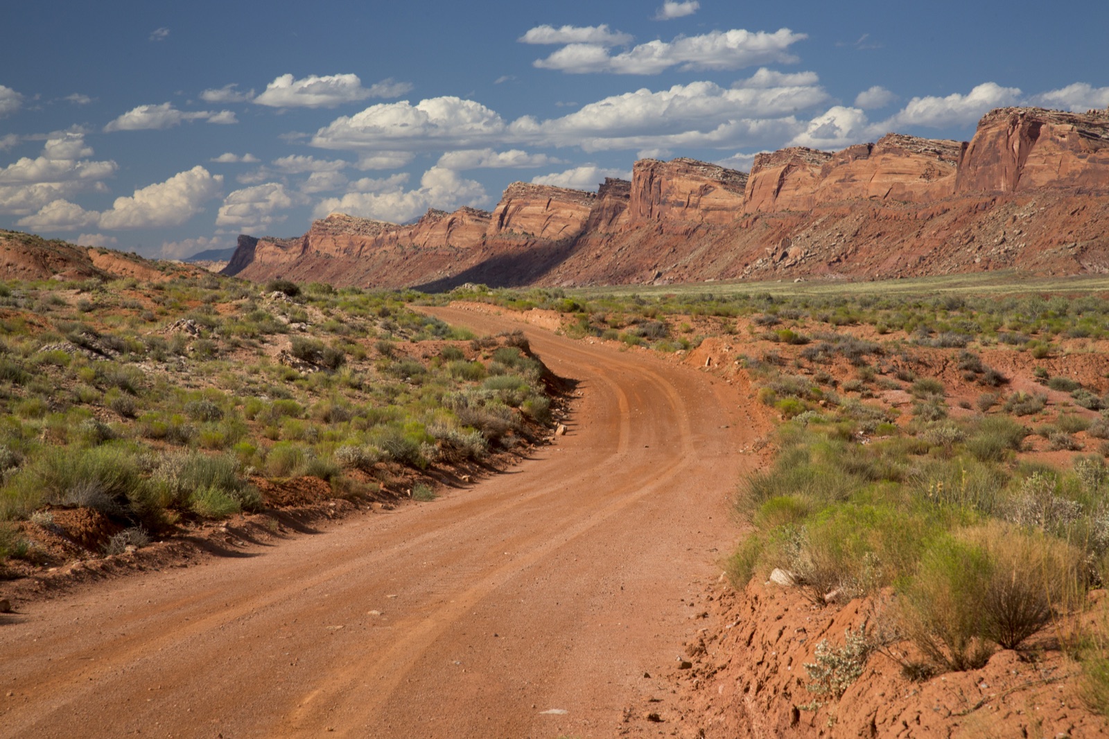 A red dirt road beneath sandstone cliffs at Lower Comb Wash in Bears Ears National Monument, Utah